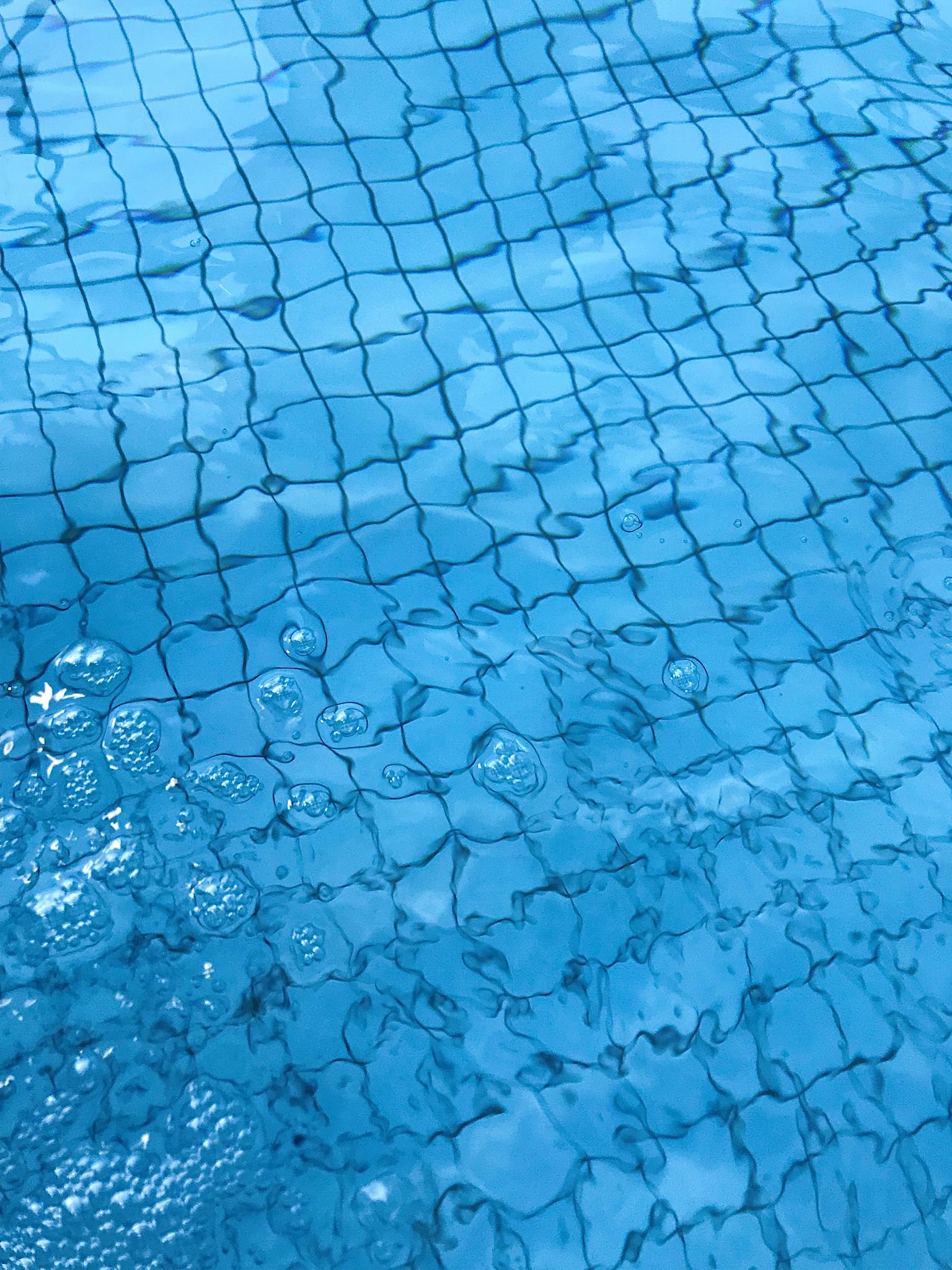 From above of transparent clean water of swimming pool with ceramic bottom in daylight